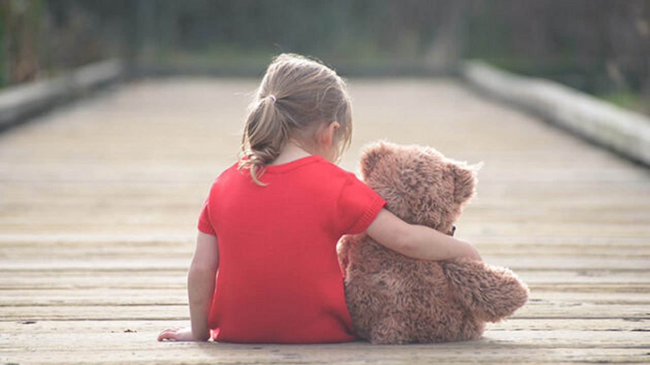 Girl in red dress sitting with teddybear on boardwalk