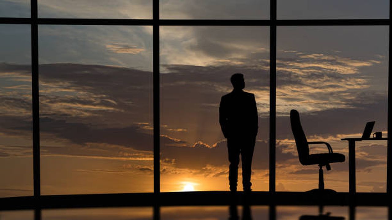 The businessman is standing near the windows in the office center