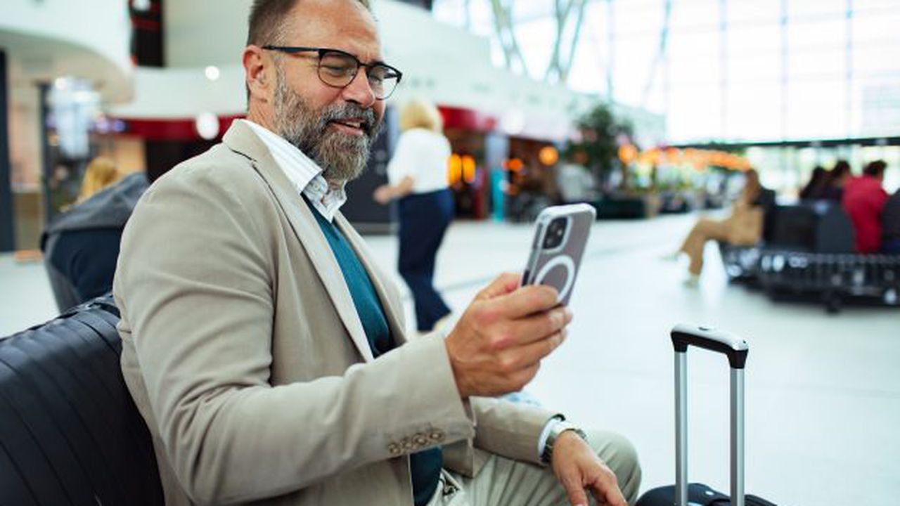 Smiling businessman using smartphone while sitting with luggage at train station